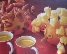 two mugs filled with orange juice next to some cut up fruit on a table