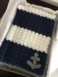 a crocheted blanket with an anchor on it in a white and blue box