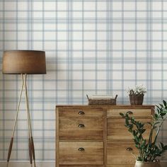 a wooden dresser sitting next to a lamp on top of a hard wood floor in front of a plaid wallpaper