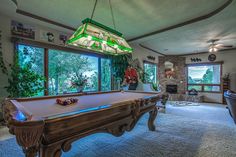 a pool table in the middle of a living room with large windows and lots of furniture