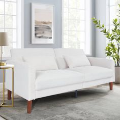 a white couch sitting in a living room next to a lamp and window sill