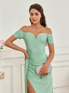 a woman in a green dress posing with her hand on her hip and wearing a silver clutch