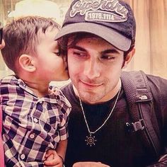 a man kissing a little boy on the cheek while he is taking a selfie