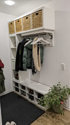 a coat rack with shoes and coats hanging on it next to a potted plant