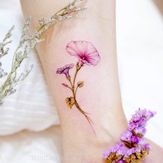 a small pink flower tattoo on the ankle and foot, with purple flowers around it