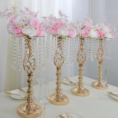 the table is set with pink and white flowers in gold vases on top of each other