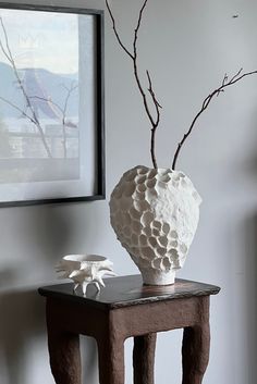 a white vase sitting on top of a wooden table next to a tree branch in a vase