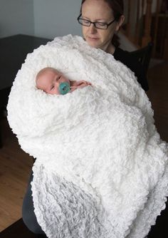 a woman holding a baby wrapped in a white blanket on top of a wooden floor