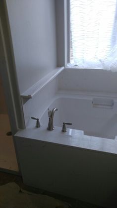 a white bath tub sitting under a window next to a sink with faucets