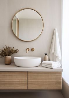 a bathroom sink with a round mirror above it and towels on the counter next to it