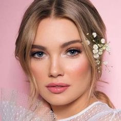 a woman with blue eyes wearing a white dress and flowers in her hair is looking at the camera