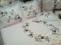 a white bed topped with lots of purple and yellow embroidered flowers next to a wooden headboard