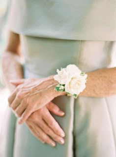 a woman in a green dress holding a white flower on her arm with both hands