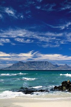 the ocean is blue with white clouds and mountains in the distance