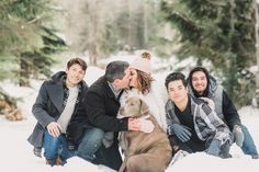 a group of people sitting next to each other in the snow with a dog on their lap