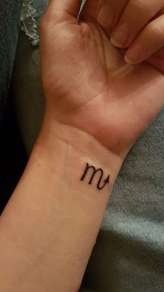 a woman's wrist tattoo with the letter m in cursive writing on it