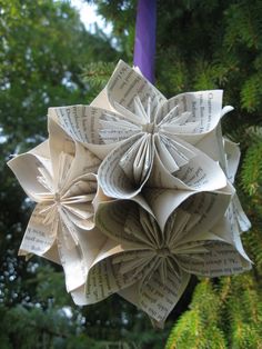 an origami flower made out of book pages hanging from a tree in front of some trees