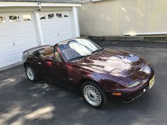 a maroon sports car is parked in front of a house with two garage doors open