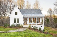 a small white house sitting on top of a lush green field with trees in the background