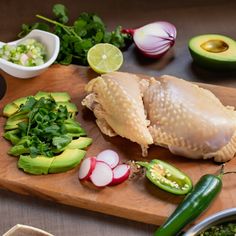 a wooden cutting board topped with chicken and veggies next to sliced avocado