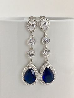 Long luxury blue sapphire cubic zirconia bridal tear dangle earrings in rhodium plated brass setting. Earrings feature a large teardrop with pear cut blue sapphire cubic zirconia center surrounded by tiny round zirconia crystals. Teardrop dangles from a bright cubic zirconia ear stud and two round cubic zirconia connectors. Total length of the earring is 6 cms. For matching necklace click: https://www.etsy.com/listing/252994446/long-blue-sapphire-cubic-zirconia-bridal?ref=shop_home_active_22 For Earrings Sapphire, Crystal Earrings Wedding, Cubic Zirconia Earrings, Ear Stud, Zirconia Earrings, Earrings Wedding, Earrings Blue, Sapphire Blue, Matching Necklaces