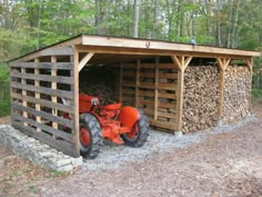 an orange tractor is parked in front of a shed made out of wood and logs