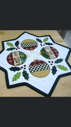 a quilted christmas ornament on a table with holly and baubles