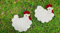 two crocheted roosters laying on the grass with their heads facing each other