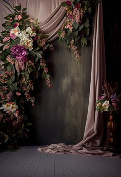 an arrangement of flowers and greenery in front of a drapeed curtain on a wooden floor