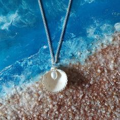 Embrace the beauty of the ocean with our handcrafted Seaside Elegance necklace, a stunning piece that captures the essence of the shore. This necklace features a natural seashell pendant, carefully selected for its unique shape and intricate patterns, paired with a lustrous freshwater pearl that adds a touch of elegance. Each necklace is lovingly handcrafted, ensuring that no two pieces are exactly alike--just like the treasures you find on the beach. The combination of organic elements and timeless pearls creates a perfect harmony, making this necklace a versatile accessory that can complement any outfit, whether you're dressing up for a special occasion or adding a touch of coastal charm to your everyday look. Features: Natural Seashell: Handpicked for its distinctive beauty, bringing th Ocean-inspired Sterling Silver Necklaces, White Shell Jewelry With Ocean-inspired Style, Sterling Silver Ocean-inspired Necklaces, Silver Shell With Pearl Pendant, White Shell-shaped Ocean-inspired Jewelry, Ocean-inspired White Shell-shaped Jewelry, Blue Round Pendant Jewelry, White Ocean-inspired Shell Necklace With Pearl Pendant, Ocean-inspired White Shell Necklace With Pearl Pendant