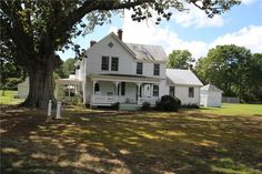 a large white house sitting in the middle of a lush green field next to a tree