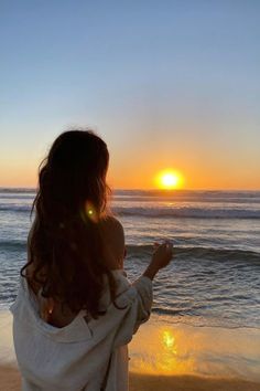 a woman standing on top of a sandy beach next to the ocean at sunset or sunrise