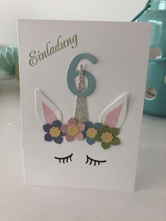 a white card with a unicorn face and flowers on it's head, the number six