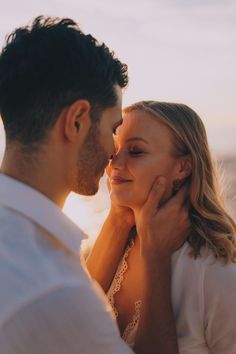 a man and woman standing next to each other in front of the ocean at sunset