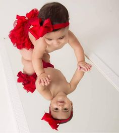 a baby girl in a red dress is reflected in a mirror with her reflection on the floor