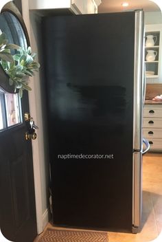 a black refrigerator freezer sitting inside of a kitchen next to a door with a potted plant on top of it