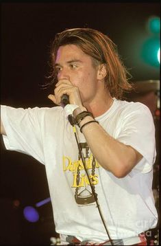 a man with long hair holding a microphone up to his mouth while standing on stage