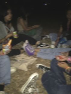 several people sitting on the ground at night with drinks and snacks in their hands,