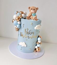 a teddy bear sitting on top of a blue cake with gold and white balloons around it