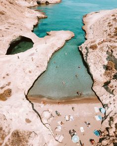 an aerial view of people swimming in the water near some rocks and sand on the beach