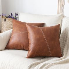 two brown pillows sitting on top of a white couch next to a wicker basket