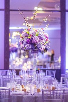 a tall vase filled with purple flowers sitting on top of a table covered in white linens