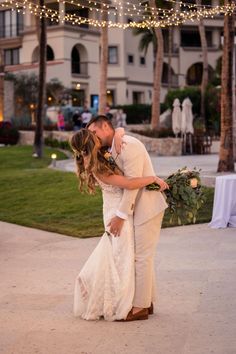 a bride and groom kissing in front of an outdoor wedding venue at dusk with string lights