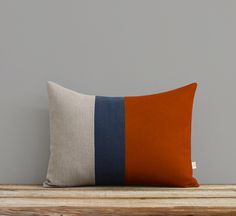 an orange and blue striped pillow sitting on top of a wooden table next to a gray wall