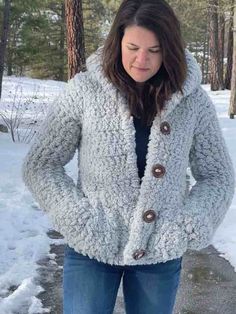 a woman standing in the snow with her hands on her hips, wearing a gray jacket and jeans