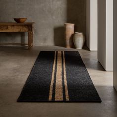 a black rug with gold stripes on the floor next to a table and vases