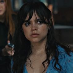 a woman with dark hair and piercings looks at the camera while another woman stands behind her