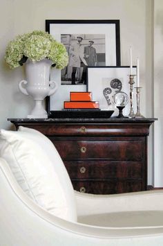 a white vase filled with flowers sitting on top of a wooden dresser next to pictures and candles