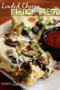 a white plate topped with pizza covered in cheese and toppings next to a bowl of tomato sauce