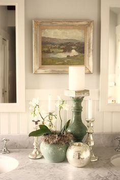 a bathroom counter topped with vases filled with flowers next to a sink and mirror